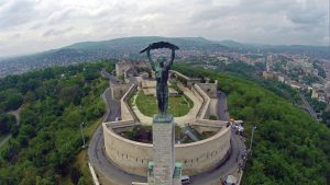 Liberty statue and Citadel on top of the green Gellért hill and the Buda hills in the background