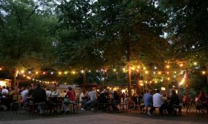The lights, tables and guests of Kertem, a garden bar in the green City park of Budapest