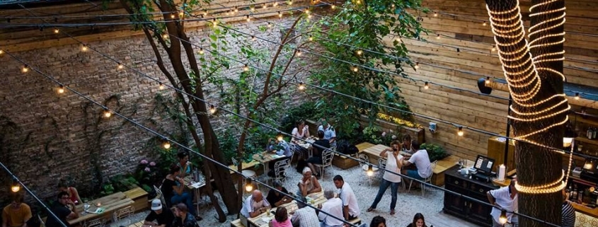 The garden of a popular bar in Budapest with tables, benches, lights and people chatting